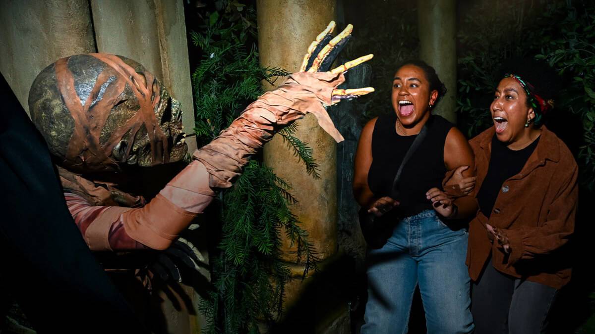 A scary actor in a mummy skull costume scaring two women